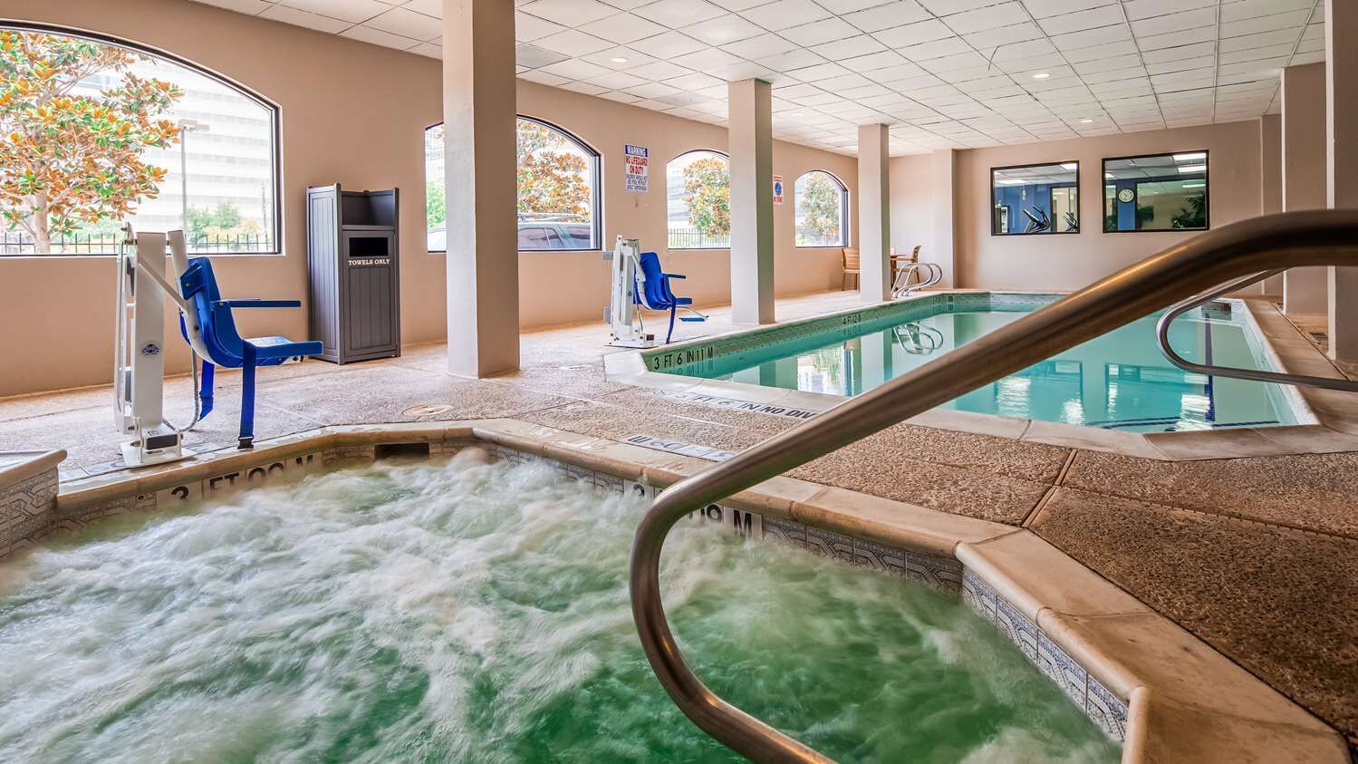 A hot tub area with a pool, seating, and a view of the outdoors.