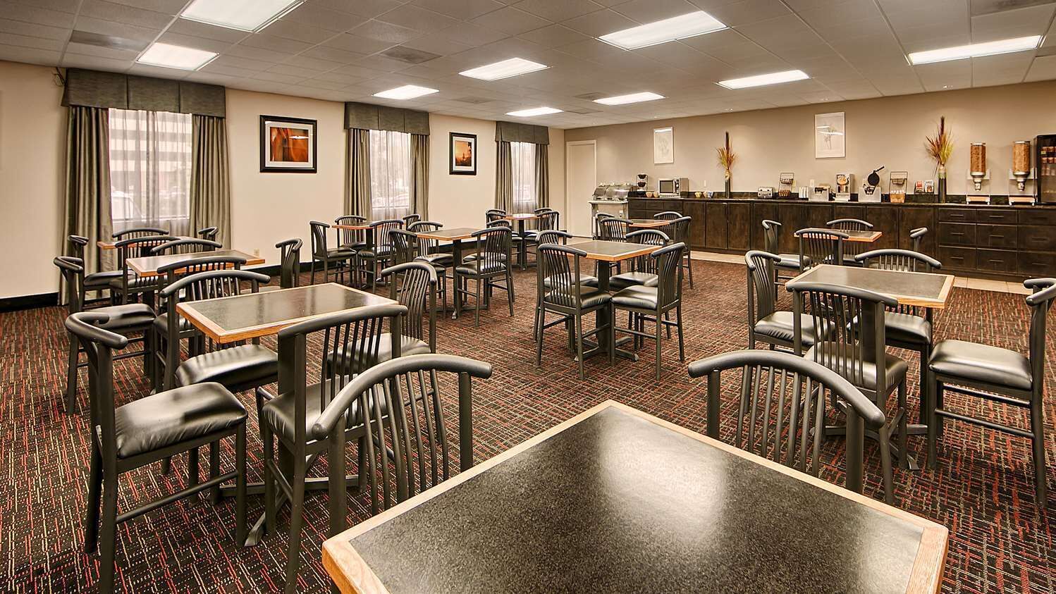 A hotel dining area with multiple tables and chairs, a counter with a coffee machine, and framed pictures on the walls.
