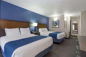 A hotel room with two beds, a nightstand, a lamp, a painting, and a mirror.