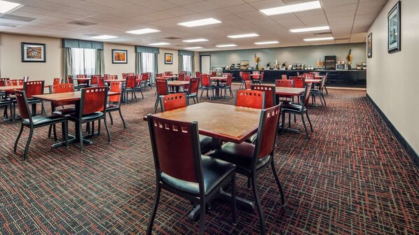 A hotel dining area with multiple tables and chairs, a counter with a beverage station, and framed artwork on the walls.