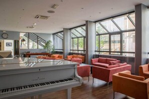 A spacious room with a grand piano, comfortable seating, large windows, and a staircase. - Hotel Atrium (Arles)