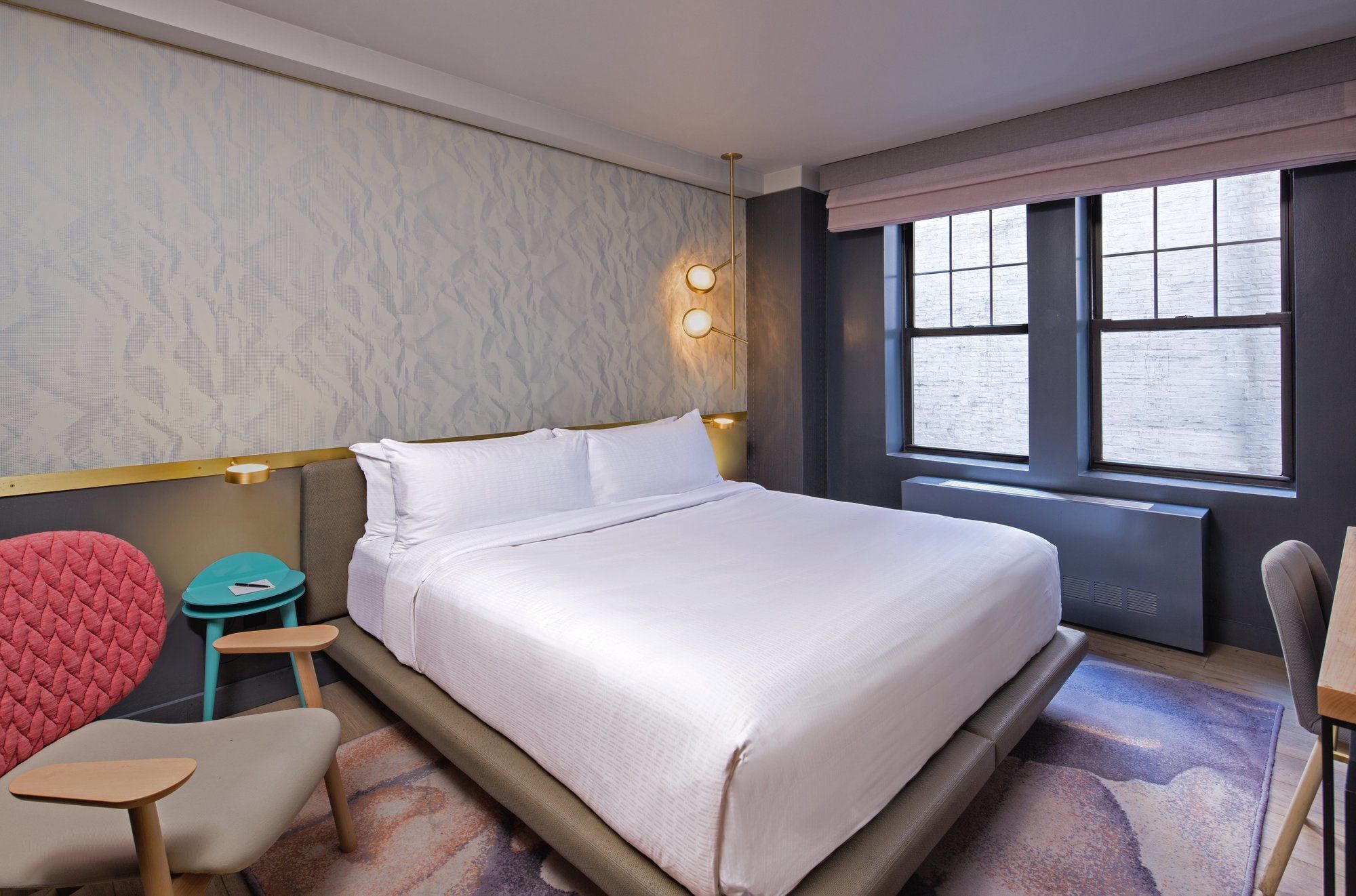 Une chambre d’hôtel moderne avec un grand lit, un coin salon comprenant un fauteuil rouge et une petite table, ainsi qu’une fenêtre donnant sur un beau paysage.