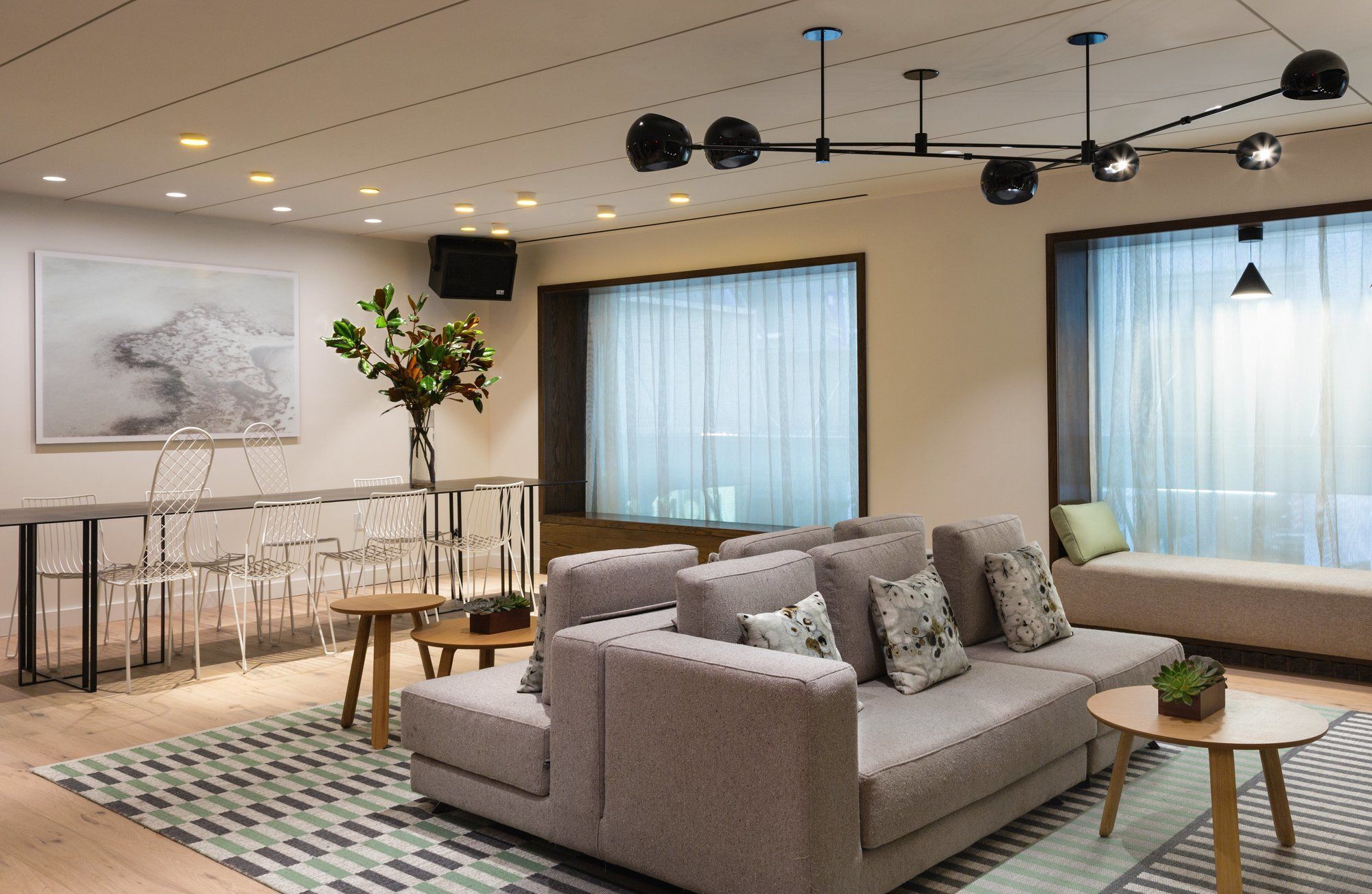 A modern living room with a sofa, a coffee table, a dining area with chairs, and a large window with sheer curtains.