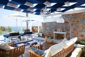 A poolside area with lounge chairs, a fireplace, and a view of the sea. - Minos Imperial Luxury Beach Resort and Spa Milatos (Agios Nikolaos)