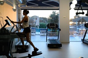 A gym with treadmills and a view of outdoor seating and a pool. - Minos Imperial Luxury Beach Resort and Spa Milatos (Agios Nikolaos)