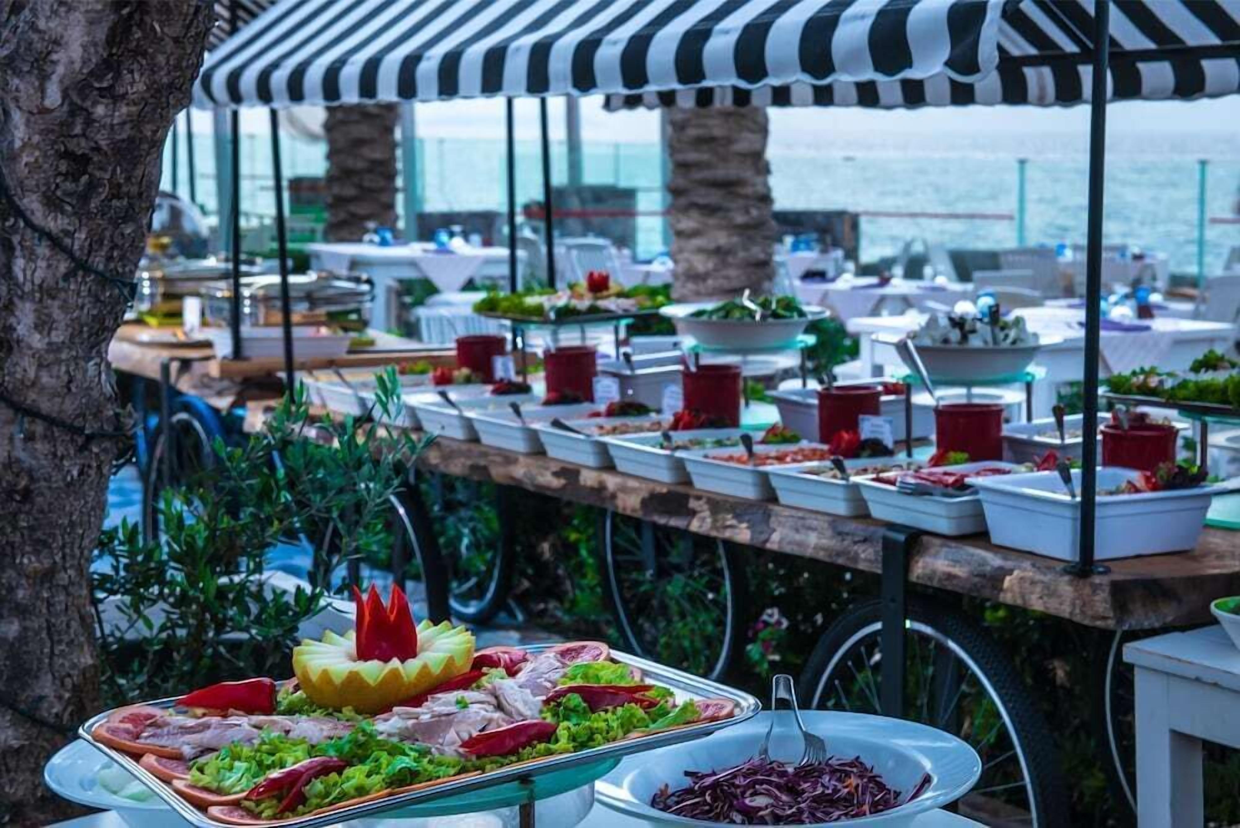 A buffet setup with various food items and a striped canopy.