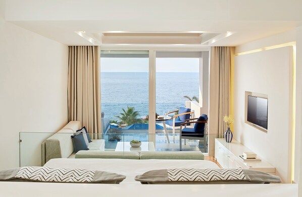 Quarto de hotel moderno com uma varanda grande, uma cama, uma televisão e vista para o mar.