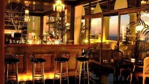 Eine Bar mit Barhocker, einer Theke voller Flaschen und Blick auf den Ozean durch große Fenster.