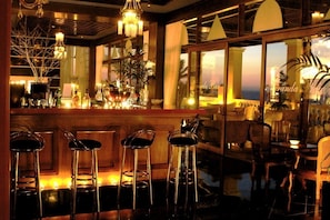 A bar area with stools, a counter with bottles, and a view of the ocean through large windows.