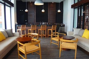 Eine Barbereich mit Holztischen und -stühlen, einer Bar mit Flaschen und einer Sitzecke mit Sofas und Sesseln.