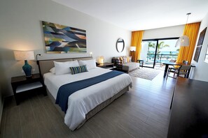 Ein Hotelzimmer mit Bett, Nachttischen, Schreibtisch, Stuhl, einem Balkon mit Meerblick und einem Bild an der Wand.