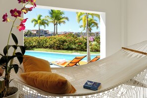 Ein Hängestuhl mit Blick auf einen Swimmingpool, Palmen und ein Gebäude im Hintergrund.