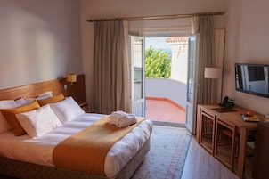 A hotel room with a bed, a desk, a television, and a balcony with a view.