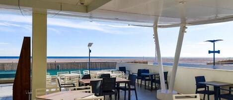 An outdoor seating area with tables and chairs, overlooking a beach.