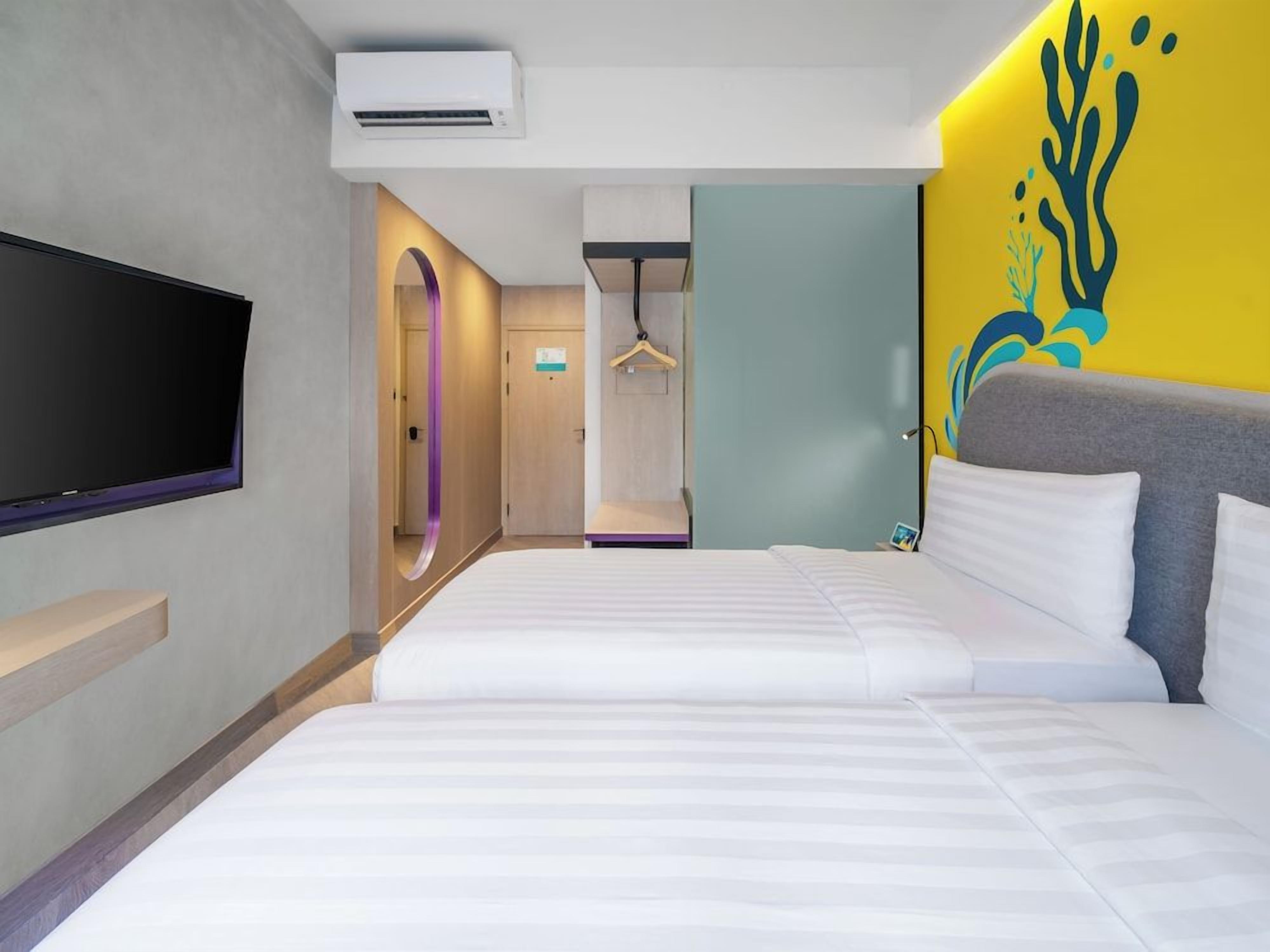 A hotel room with two beds, a TV, an air conditioner, and a hallway with a door.