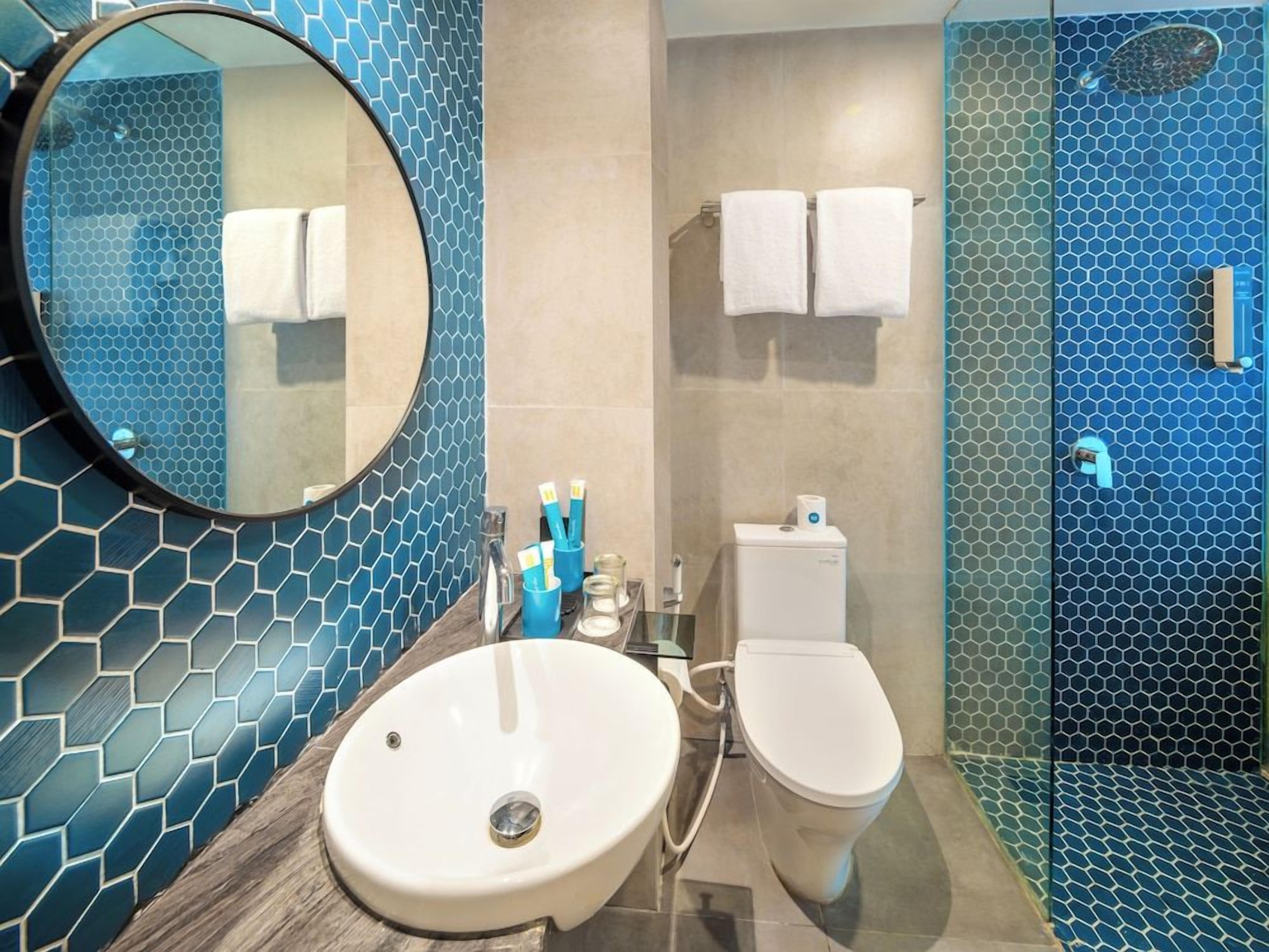 A bathroom with a round mirror, a sink, a toilet, and a shower.