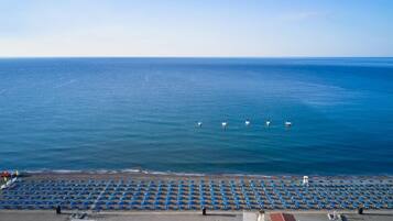 A beach with rows of blue umbrellas and a few boats in the water.