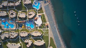 An aerial view of a resort with multiple swimming pools, a beach with umbrellas, and a coastline.