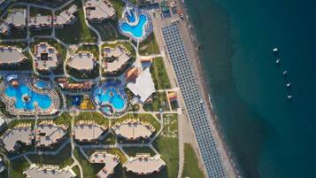 An aerial view of a resort with multiple swimming pools, a beach with umbrellas, and a coastline.