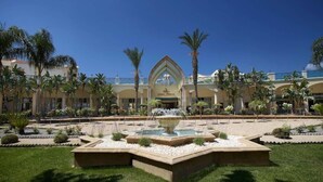 A hotel with a central fountain, palm trees, and a clear blue sky.