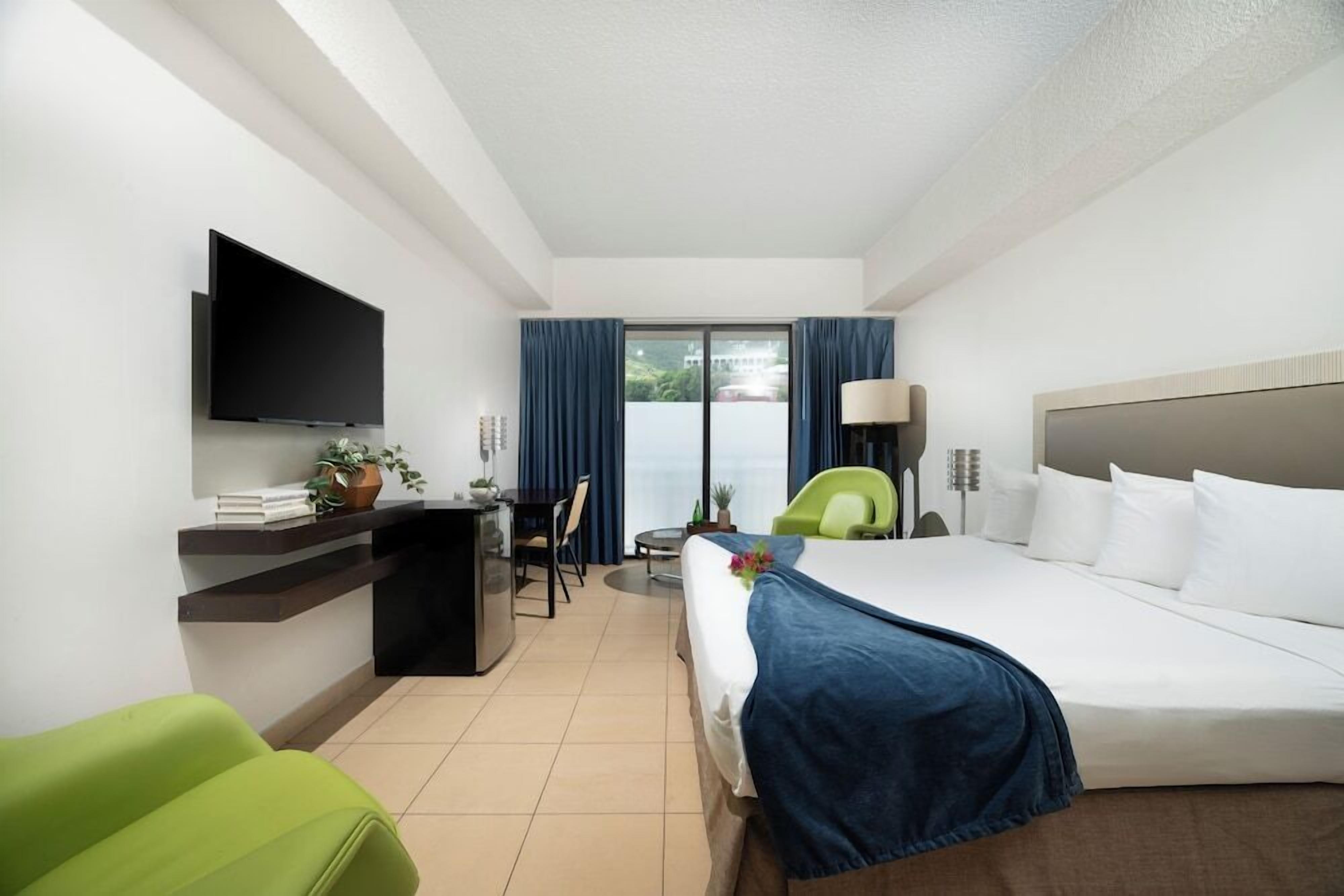 Ein Hotelzimmer mit Bett, Schreibtisch, Stuhl, Fernseher und einem Fenster mit Vorhängen.
