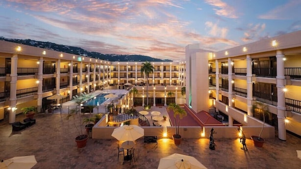 Un hotel de varios pisos, con un patio central con piscina, mobiliario exterior y vistas del paisaje circundante.