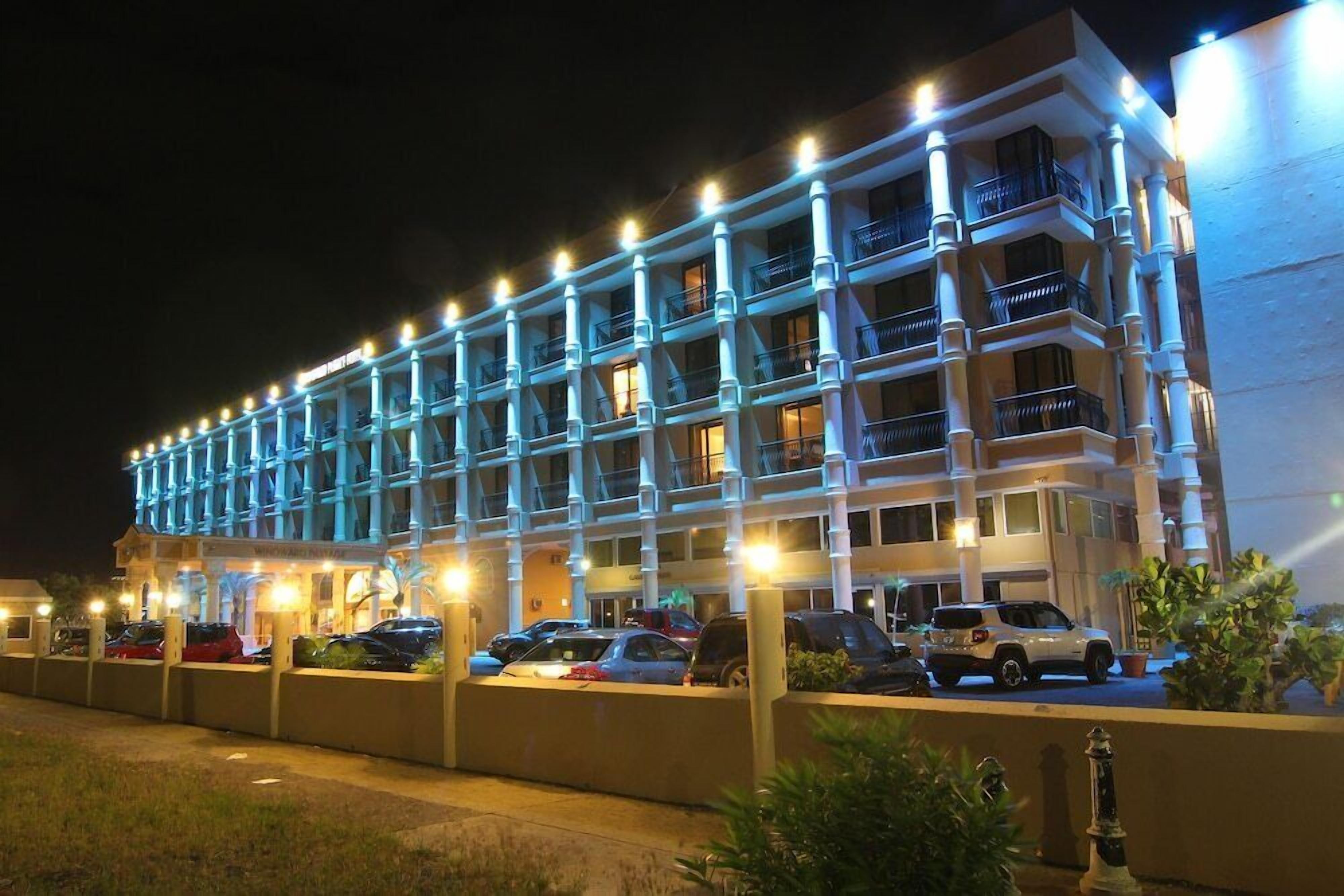 Un hotel de varios pisos con balcones, un estacionamiento y una fachada bien iluminada.