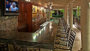 Una zona de bar con una barra larga, armarios de madera y una pantalla de televisión.