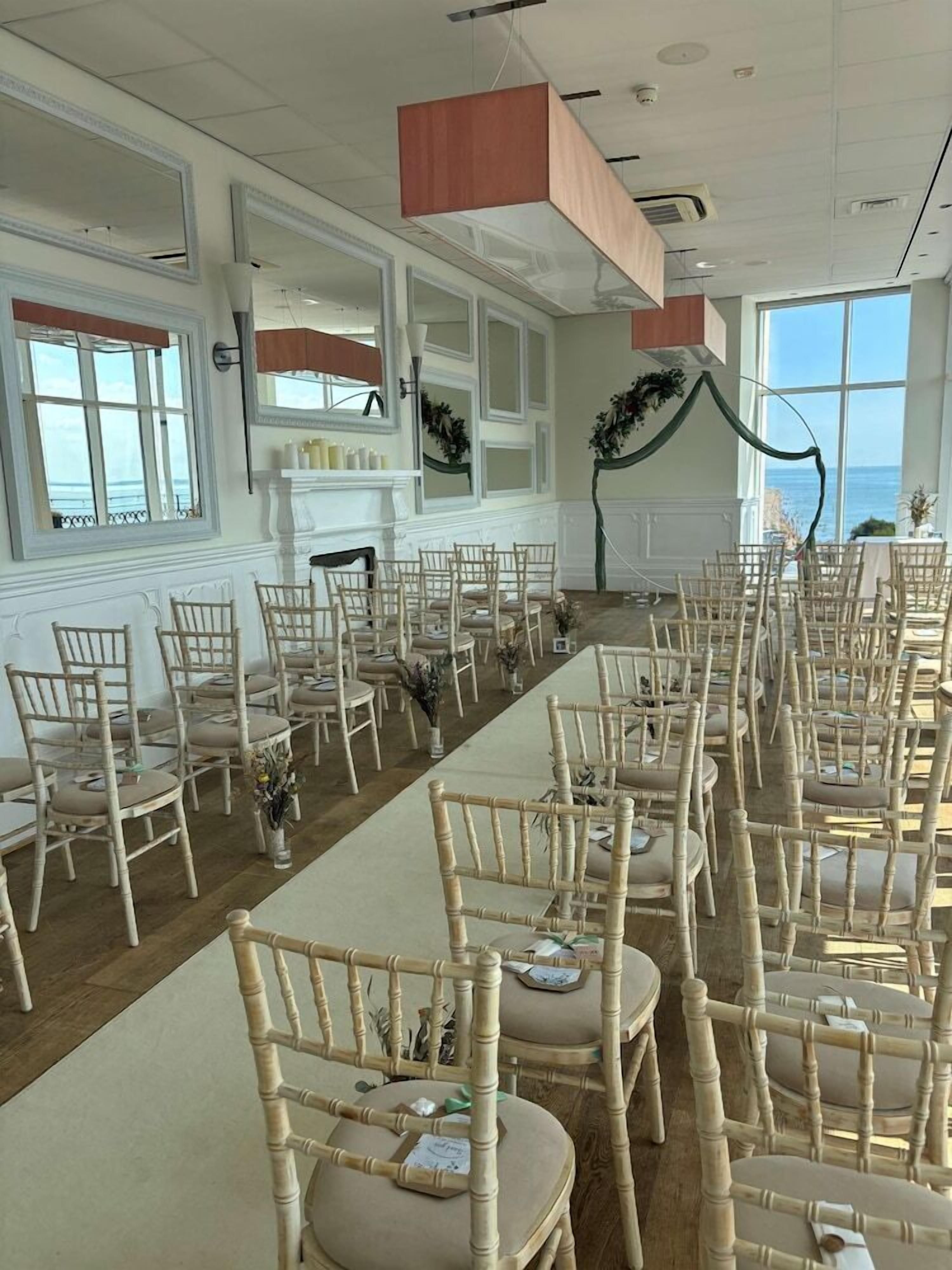 Uma longa mesa de banquete com cadeiras dispostas ao redor, uma lareira e janelas amplas com vista.