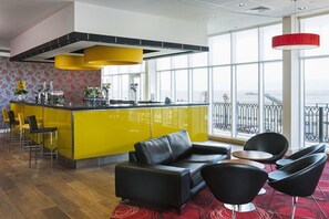 A modern bar area with yellow accents, a black leather sofa, and a view of the sea through large windows. - Park INN BY Radisson Palace Southend ON SEA (Southend-on-Sea)