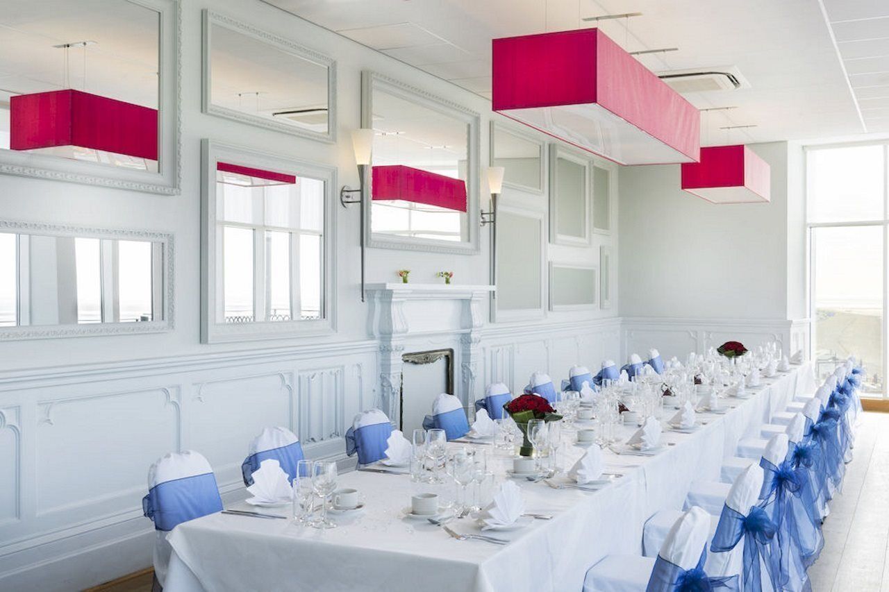 A long dining table set for a formal event with white tablecloths, blue sashes, and red flowers.