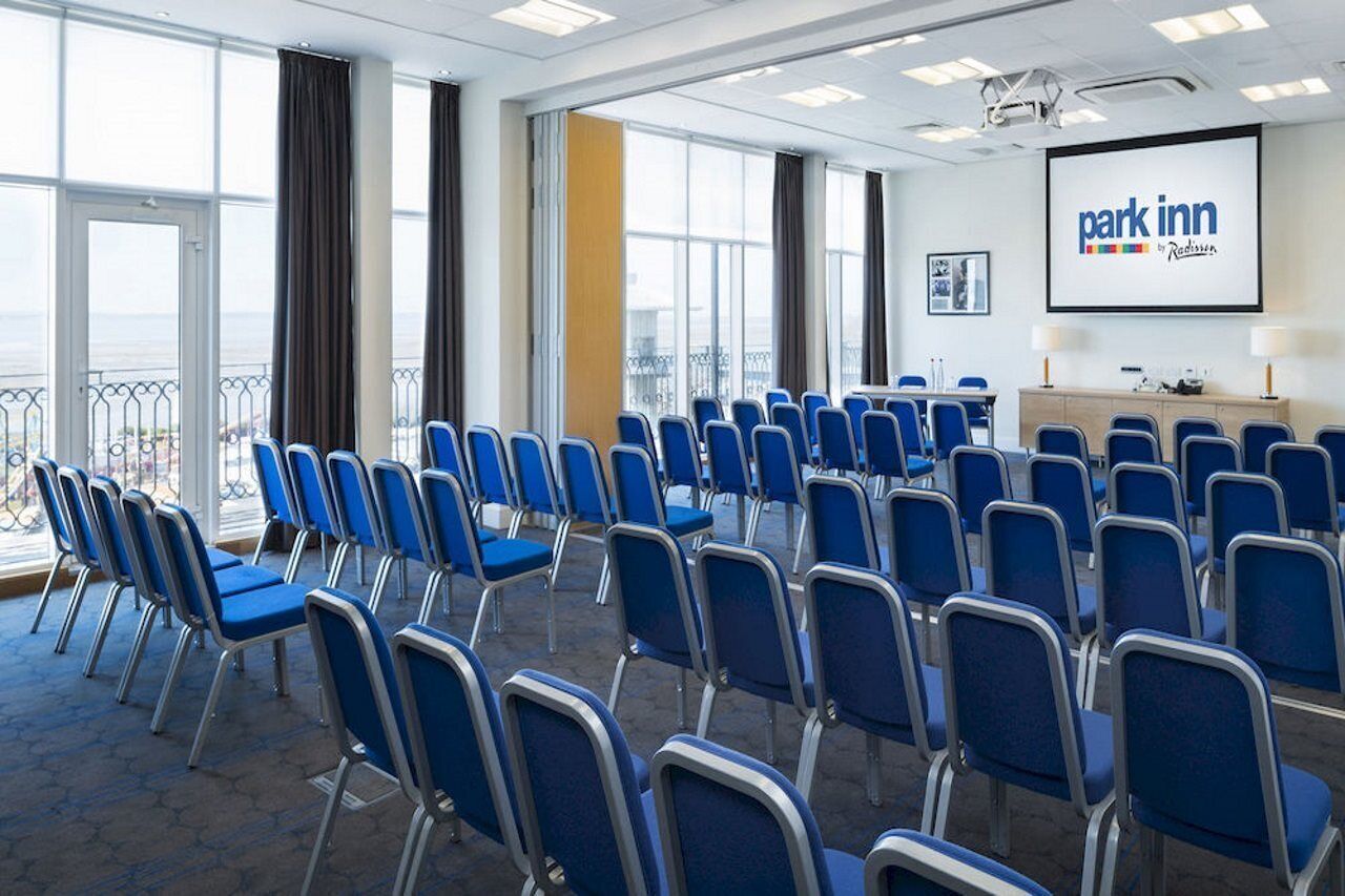 A conference room with rows of blue chairs, a projector screen, and a large window with a view.