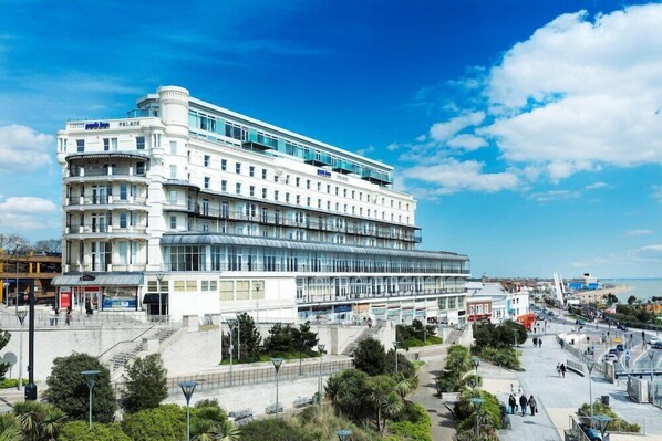 Un hotel de varios pisos con diseño moderno, que cuenta con balcones, ventanas amplias y un patio central.