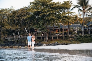 A couple standing by a body of water with a wooden fence and trees in the background.