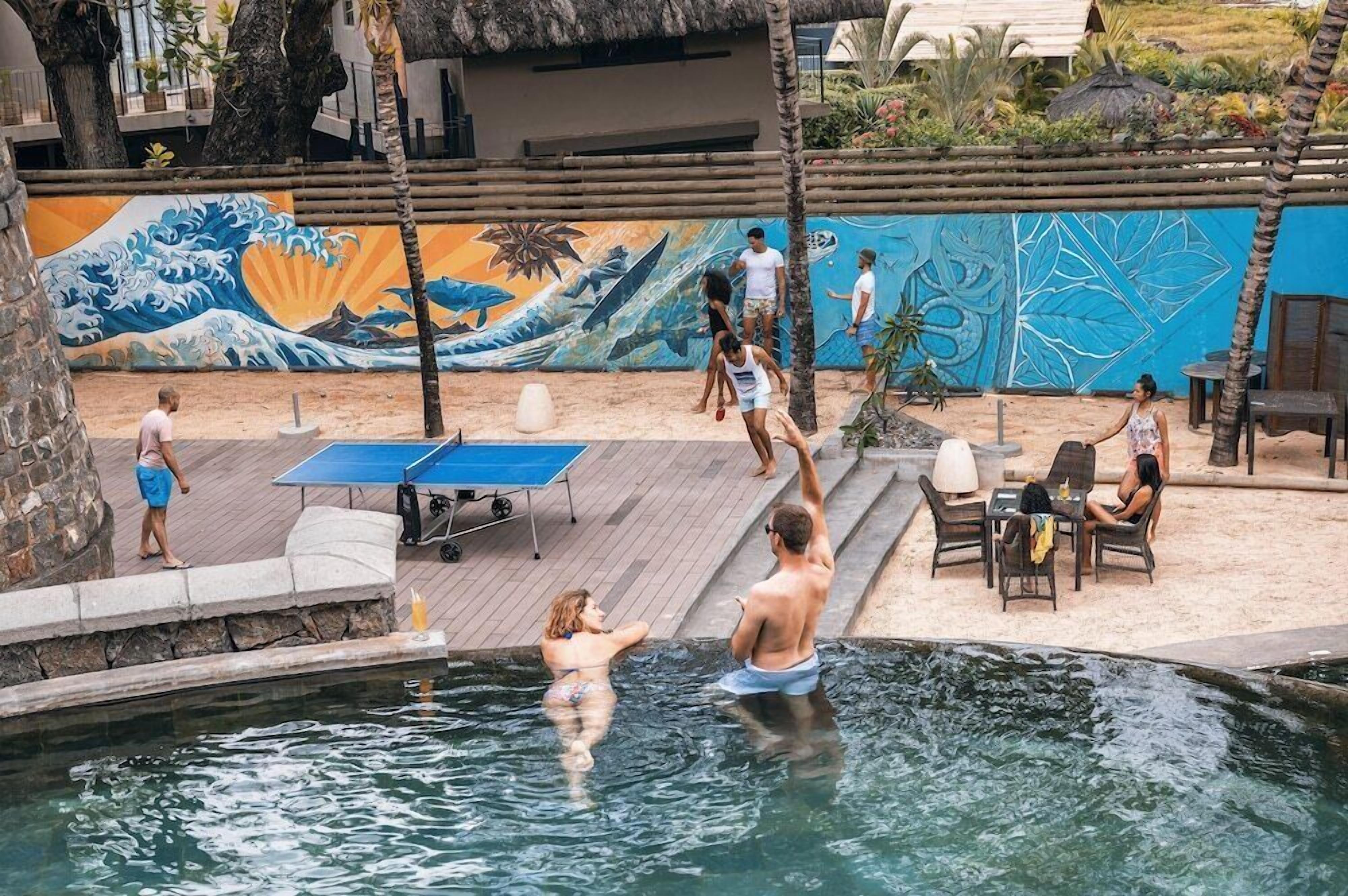 Un espace piscine agrémenté d’une fresque murale, de coins salon extérieurs et d’une table de ping-pong.