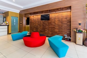 A modern lobby with a wooden wall, a flat-screen TV, and blue and red seating. - Kingston Hotel 12 @ Jalan Raja Laut, KL (Kuala Lumpur)