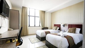 Habitación de hotel con dos camas, un escritorio, una silla, un televisor y una ventana con cortinas.