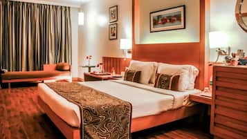 A hotel room with a large bed, a desk, a chair, a nightstand, and a window with curtains.