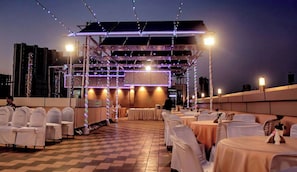 An outdoor event space with tiered seating, string lights, and tables set for dining. - Hotel Heritage (Mumbai)