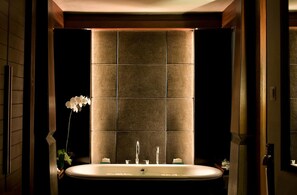 A modern bathroom with a freestanding bathtub, a large mirror, and a wall-mounted sink. - The Kayana Seminyak Bali (Seminyak)