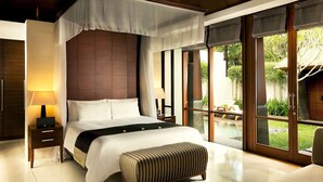 A bedroom with a canopy bed, a bedside table with a lamp, a bench, and large windows with a view of the outdoors.