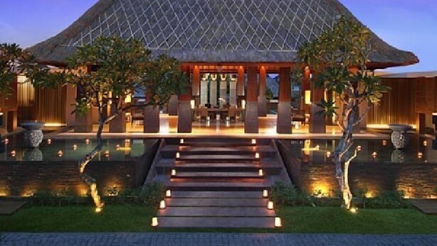 A modern building with a large, pyramid-shaped roof, a central courtyard with steps leading to a seating area, and water features surrounding the space.