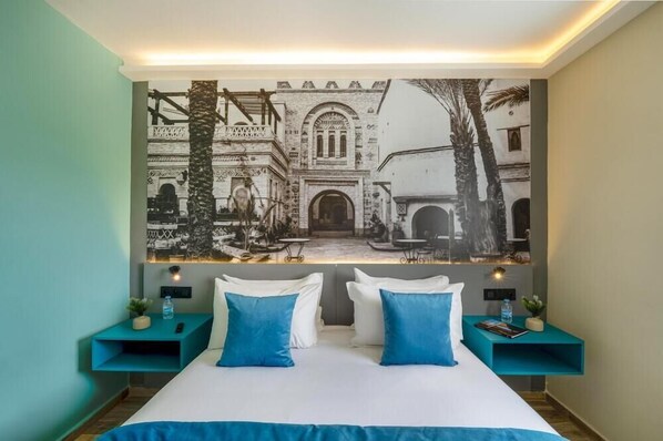 A hotel room with a bed, two nightstands, a large wall-mounted picture, and a teal accent wall. - MIA Urban Agadir (Agadir)