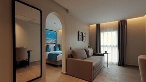 A modern hotel room with a large mirror, a sofa, a small table, and a bed with a cityscape view. - MIA Urban Agadir (Agadir)