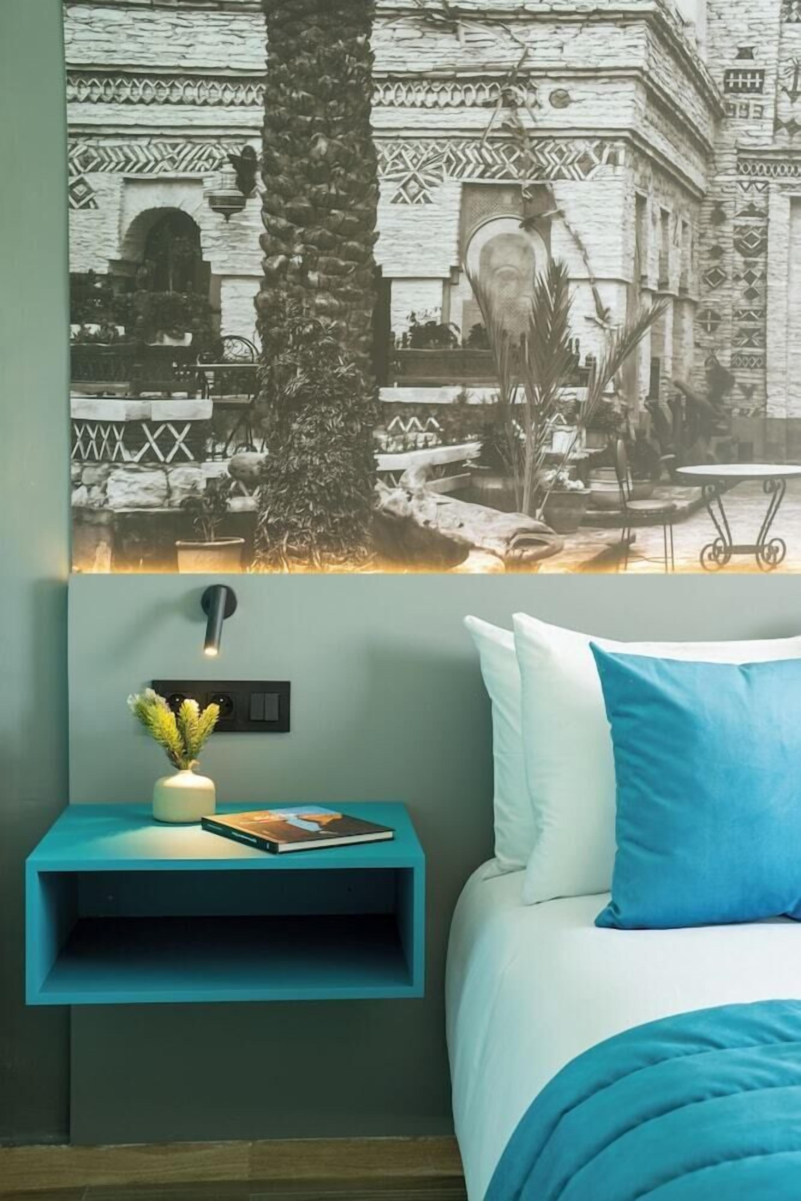 Une chambre à coucher comprenant un lit, une table de chevet avec une lampe, une prise de courant murale et un élément décoratif fixé au mur.