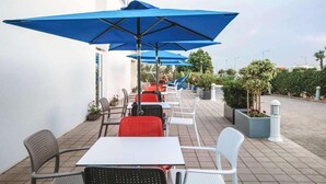 An outdoor seating area with tables and chairs, blue umbrellas, and potted plants. - MIA Urban Agadir (Agadir)