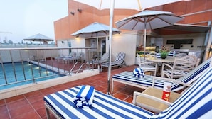 Un área de piscina en la azotea con sillones, sombrillas y un comedor.