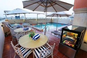 En bar på taket med en pool, solstolar, parasoller och en minibar.
