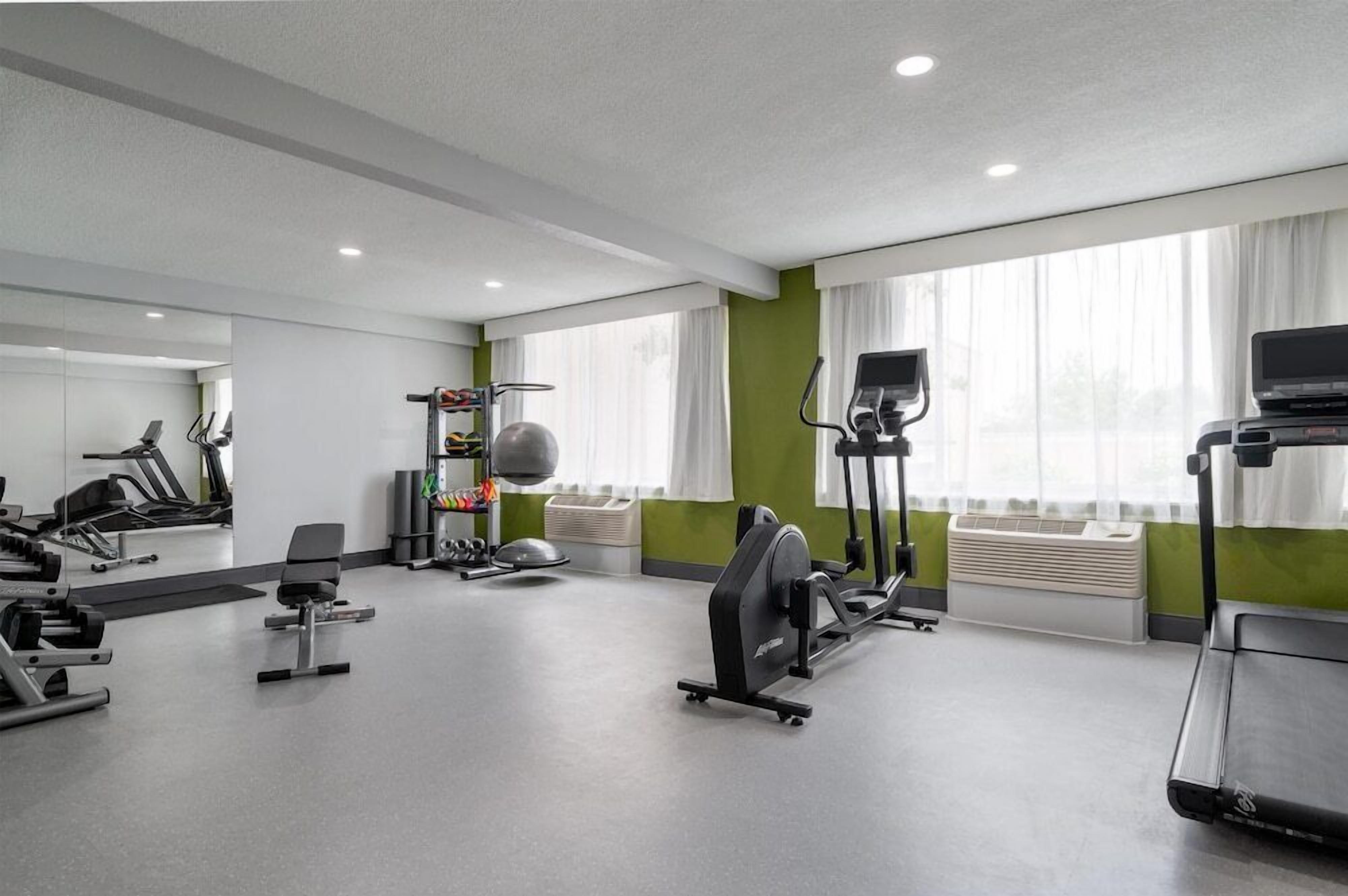 Un gimnasio con máquinas de cardio, pesas y un espejo grande.