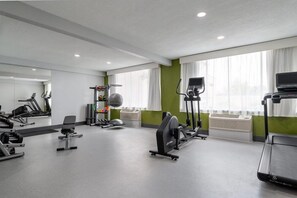 Une salle de sport équipée de machines de cardio, de poids libres et d’un mur avec des miroirs.
